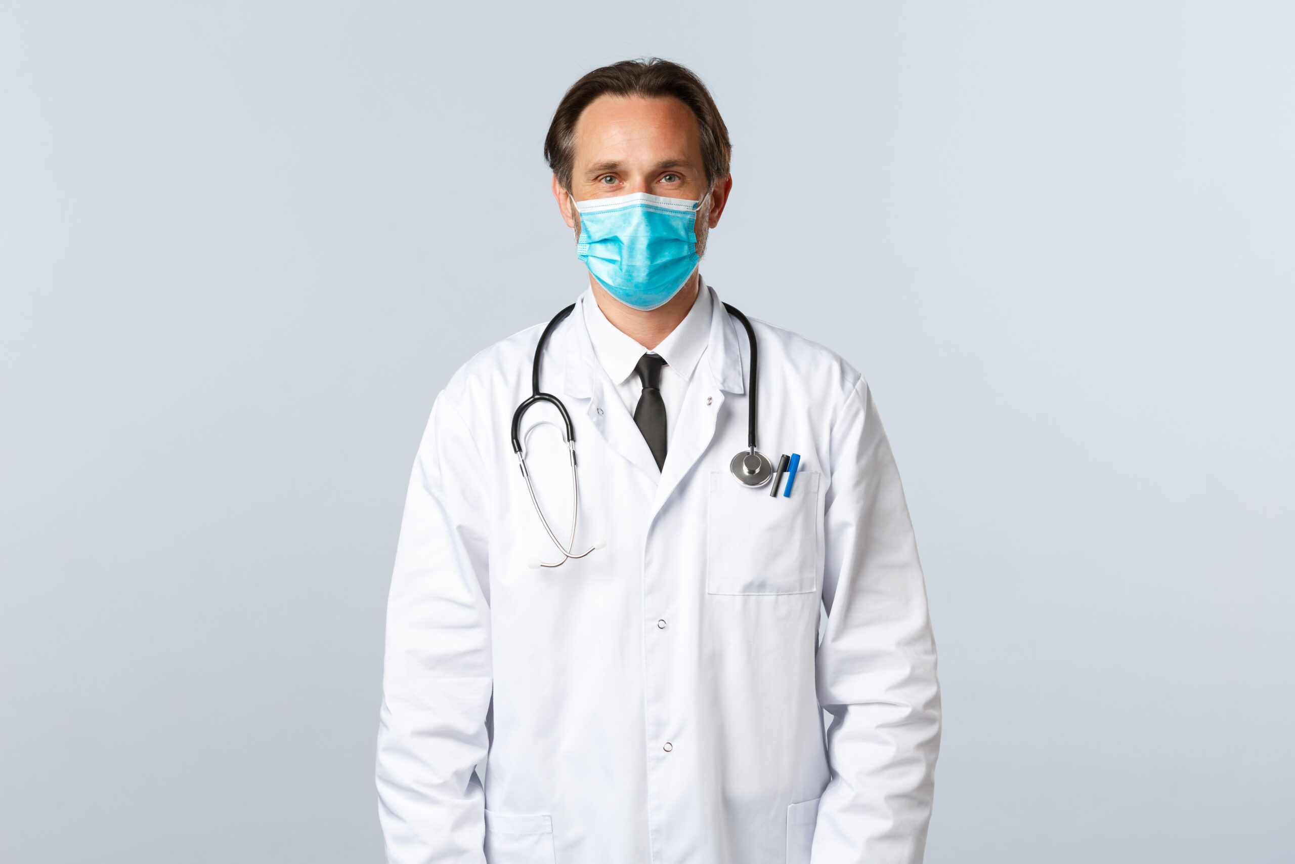 covid 19, preventing virus, healthcare workers and vaccination concept. middle aged professional therapist in white coat and medical mask listening to patient in clinic, doctor at work